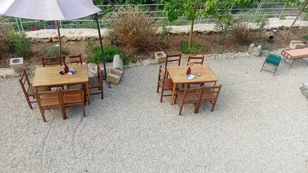 Dos mesas de madera con sillas, un paraguas grande y suelo de grava.