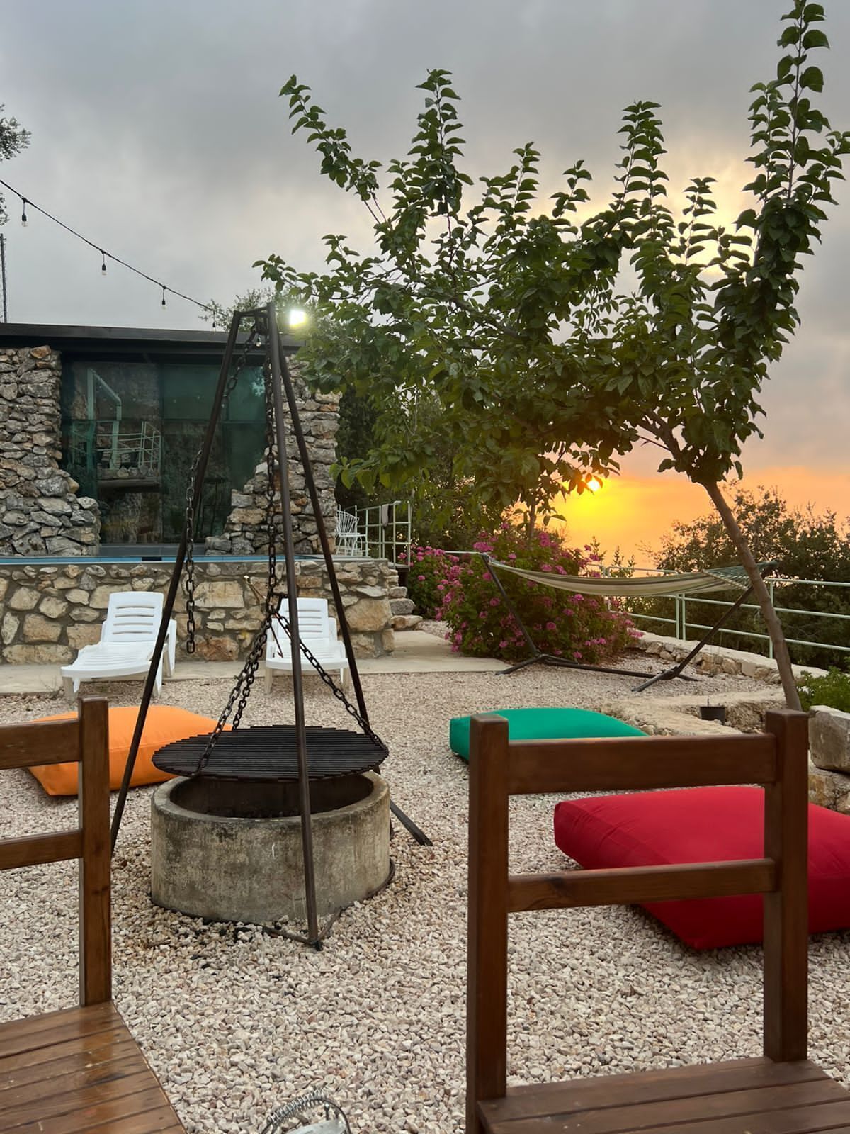An outdoor seating area with a fire pit, lounge chairs, and a view of the sunset.