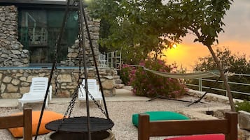An outdoor seating area with a fire pit, lounge chairs, and a view of the sunset.