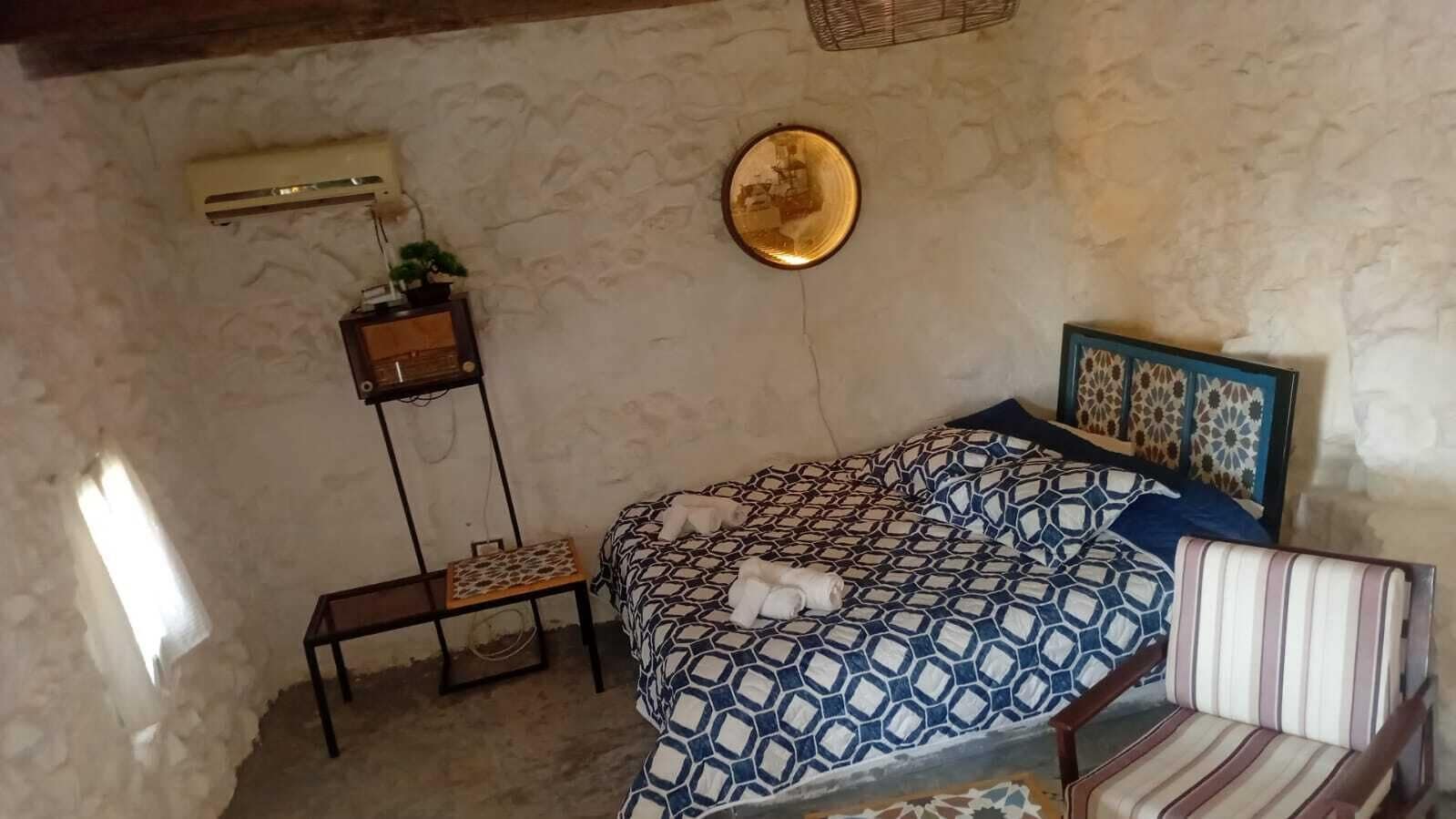 Une chambre à coucher comprenant un lit, une table de chevet, une chaise, un climatiseur fixé au mur et une assiette décorative.