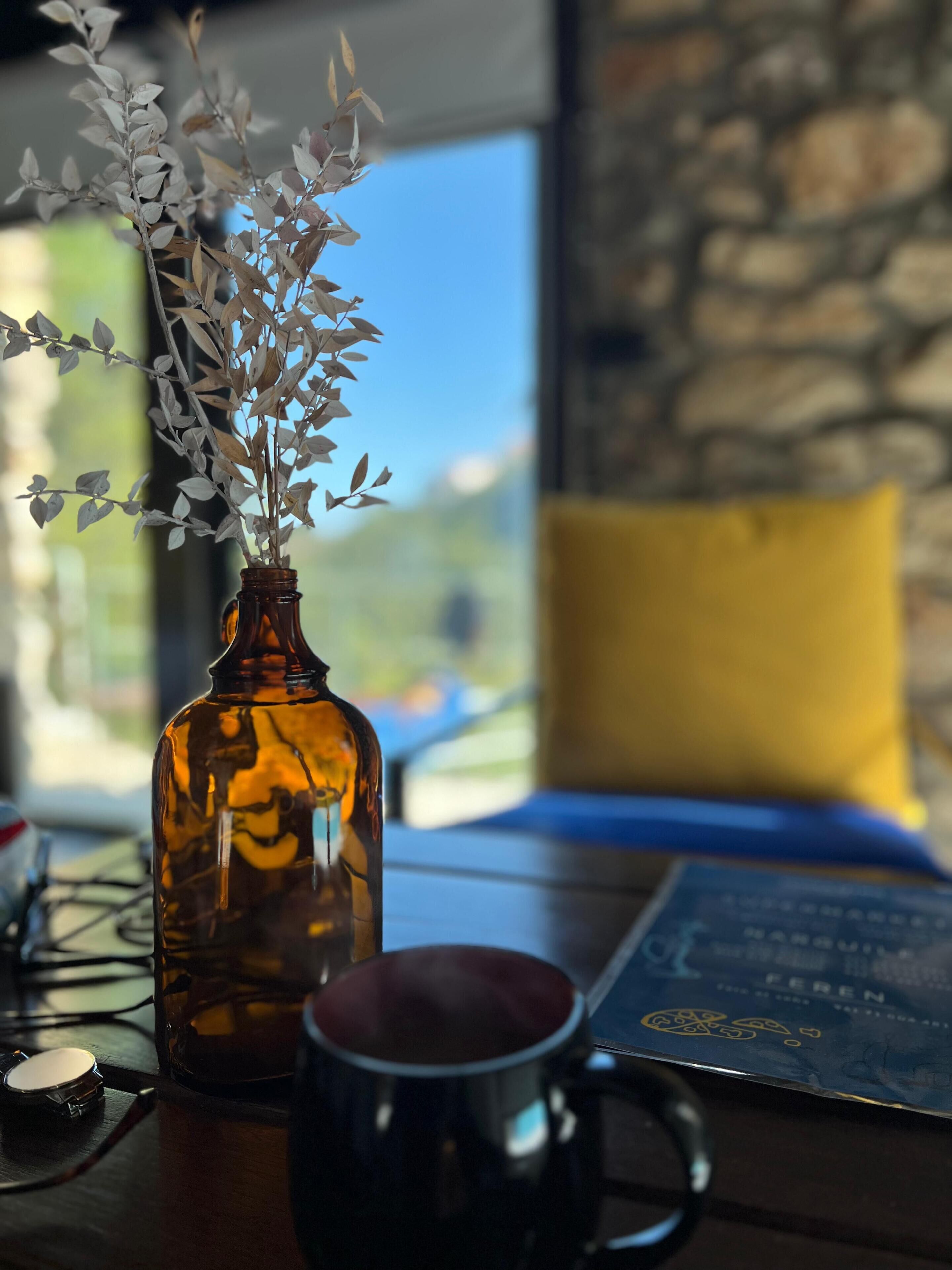 A brown glass bottle with a plant, a dark mug, and a menu on a wooden table.