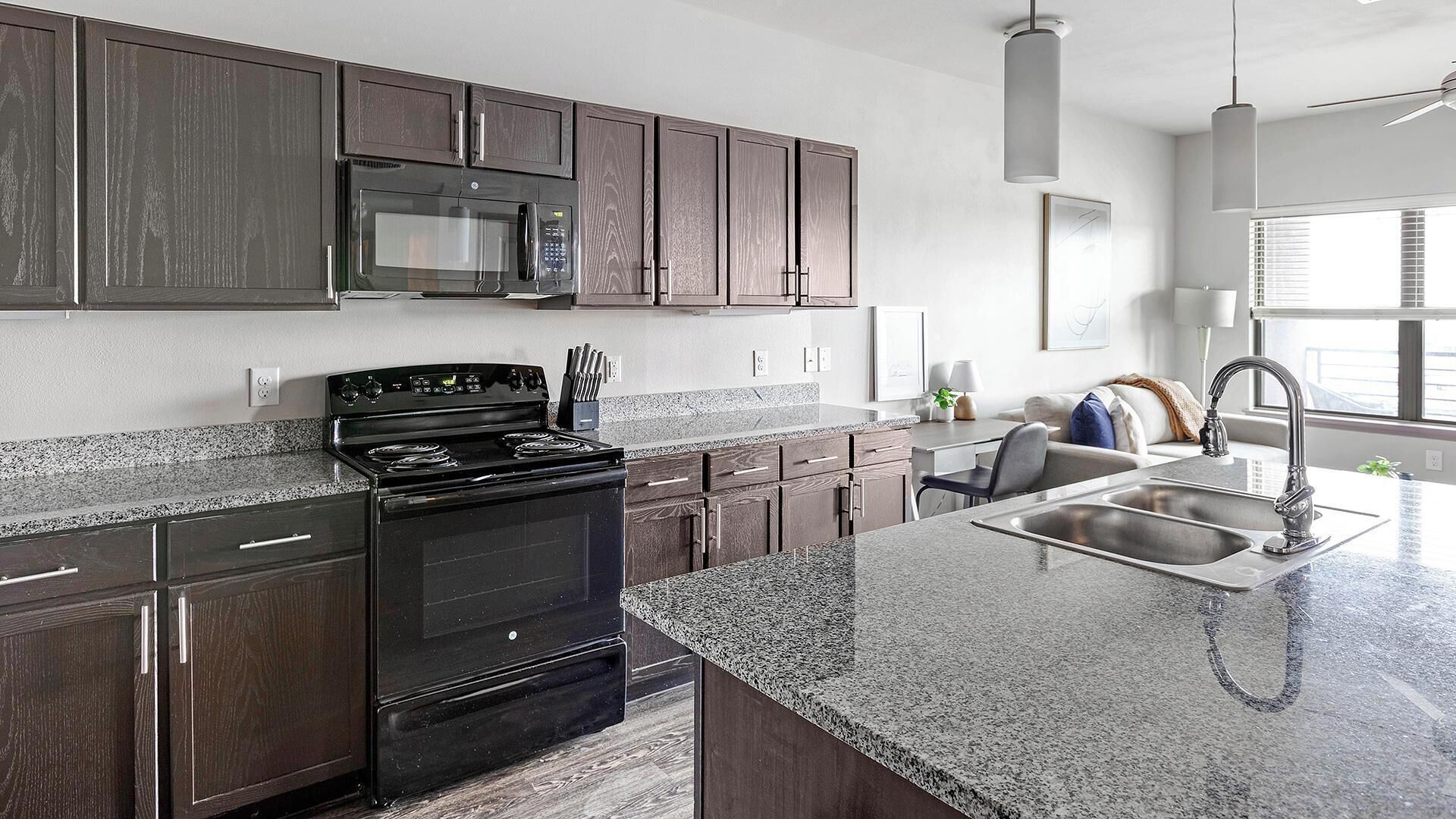 A modern kitchen with dark wood cabinets, a stainless steel sink, and a granite countertop.
