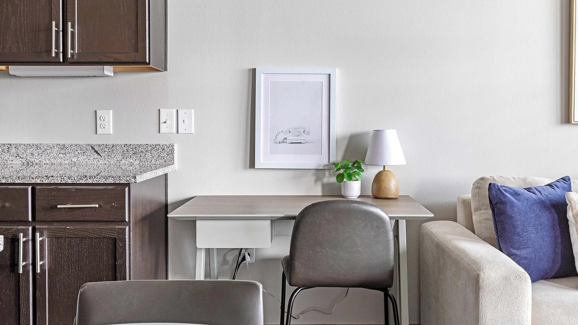 A modern living room with a grey sofa, a coffee table, and a desk with a lamp and a framed picture.