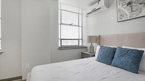 Een slaapkamer met een bed, nachtkastje, lamp en een raam met jaloezieën.