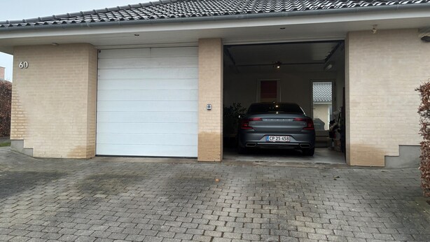 A garage with a car parked inside, a white garage door, and a brick wall with the number 60 visible. - House close to Roskilde Center (Roskilde)