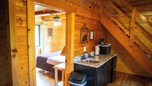 Une cabane confortable avec un intérieur en bois, une petite cuisine, un lit et un escalier.
