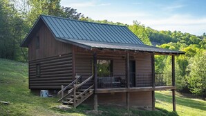 Une cabane rustique avec un toit en métal, un revêtement extérieur en bois et une véranda dotée d’une balustrade.