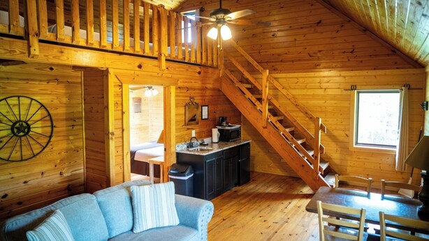 L’intérieur chaleureux d’un chalet avec un escalier en bois, un coin repas, une cuisine et un salon doté d’un canapé.