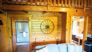 L’intérieur d’un chalet accueillant, avec un mur en bois, un élément décoratif circulaire en bois, un canapé avec des coussins et une porte visible donnant sur une autre pièce.