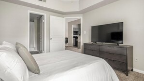 A bedroom with a bed, a dresser, a TV, and a door leading to a bathroom.