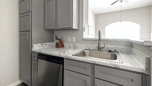 A modern kitchen with grey cabinets, a stainless steel dishwasher, and a marble countertop.