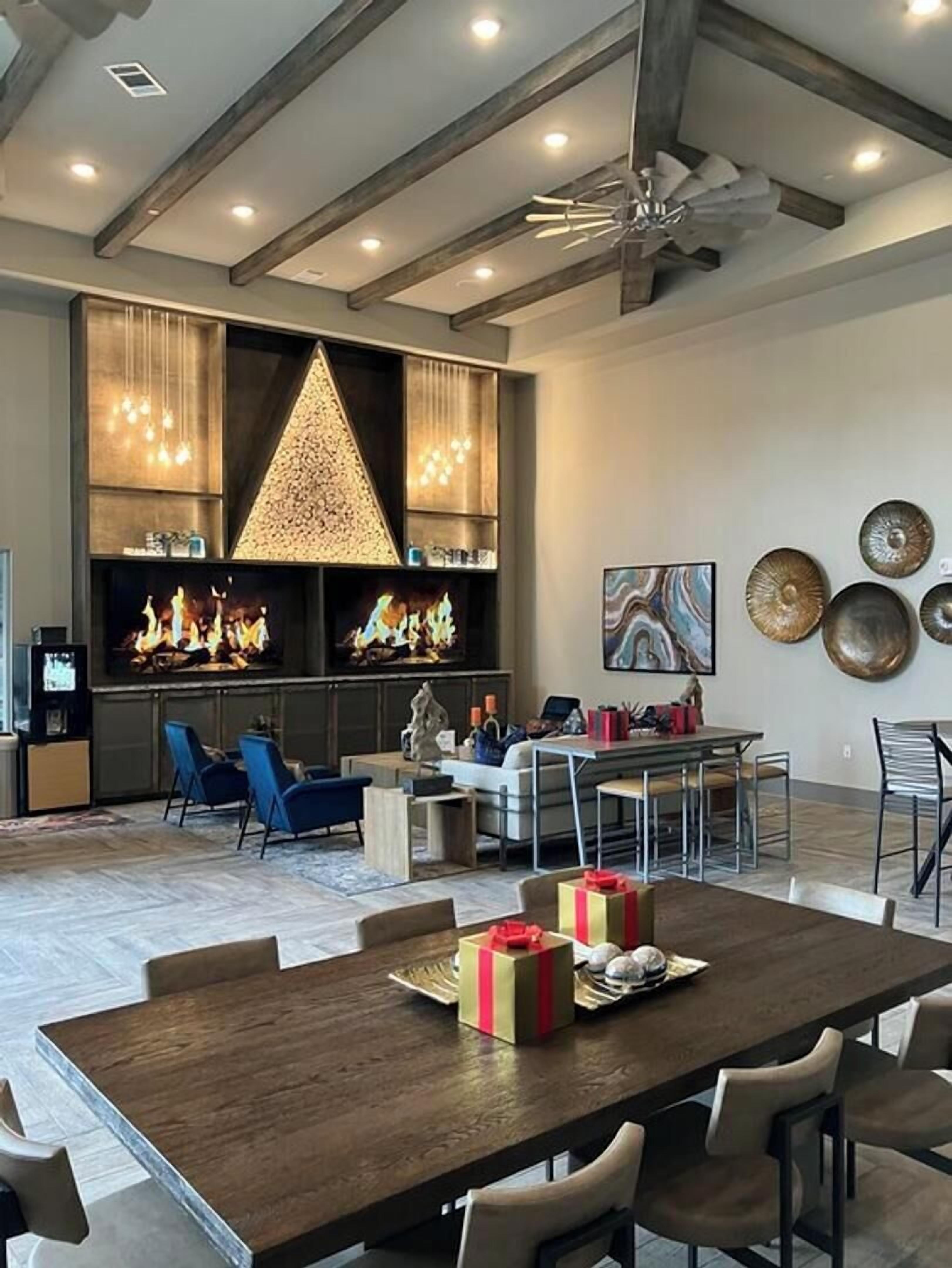 A spacious living area with a large wooden dining table, blue chairs, a fireplace, and a modern ceiling fan.