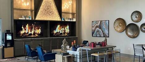 A spacious living area with a large wooden dining table, blue chairs, a fireplace, and a modern ceiling fan.