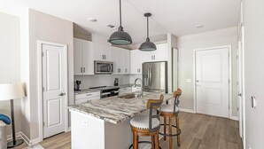 A modern kitchen with white cabinets, a granite countertop, a stainless steel refrigerator, and a two-bench dining area.
