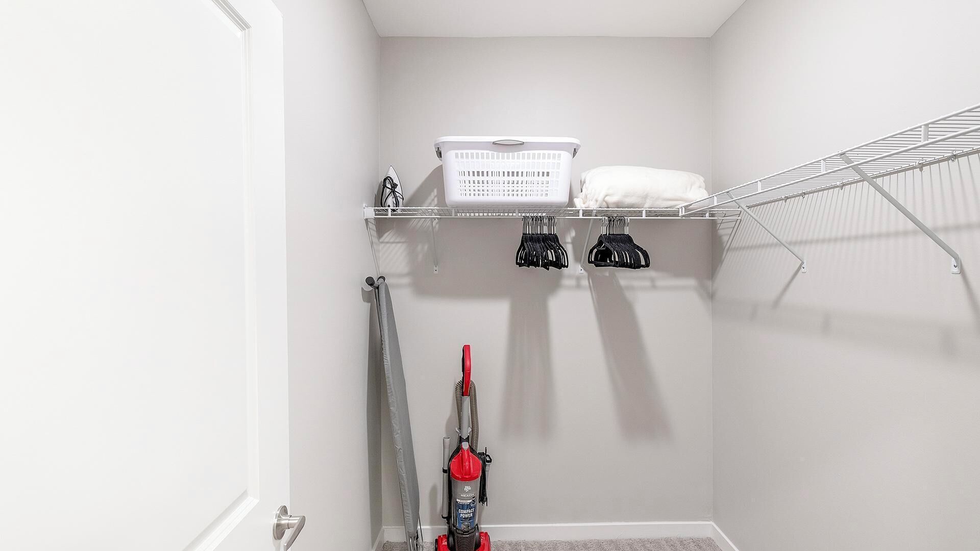 A compact, white closet with shelves for storage, a hanging rack, and a vacuum cleaner.