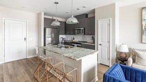 A modern kitchen with a central island, bar stools, and pendant lighting.