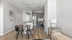 Eine moderne Küche mit Edelstahlgeräten, ein Essbereich mit Holztisch und Stühlen sowie ein Wohnbereich mit Sofa und Lampe.