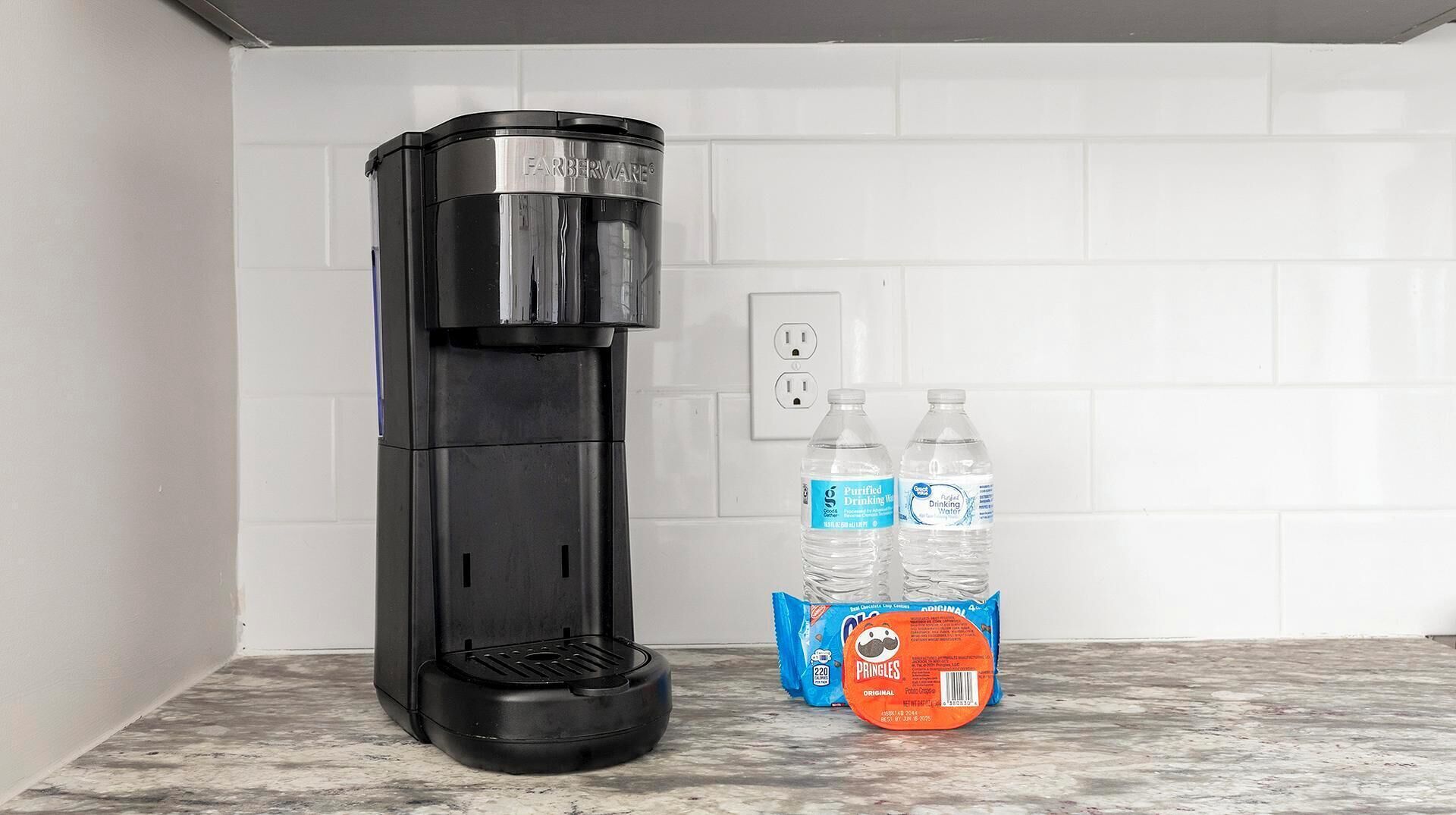 A kitchen with a black coffee maker, two water bottles, and a bag of Pringles.