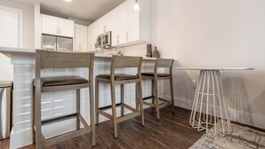 A modern kitchen with white cabinets, a stainless steel refrigerator, and wooden bar stools.