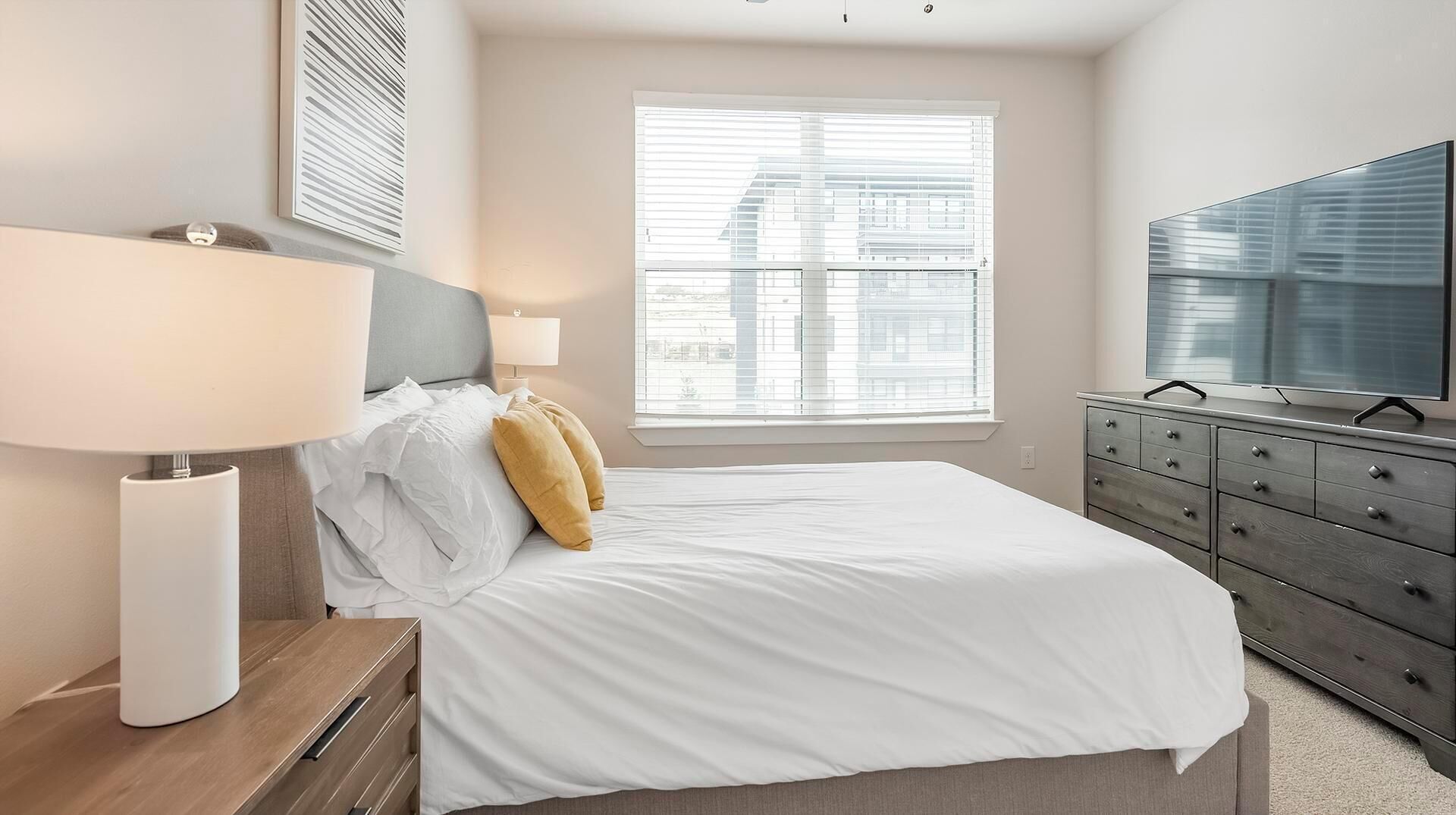 Un dormitorio con cama, cómoda, televisor y ventana con persianas.