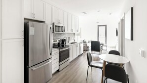 Una cocina moderna con electrodomésticos de acero inoxidable, un comedor con una mesa redonda y sillas, y vistas a través de un ventanal.