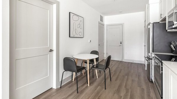 A modern kitchen with a dining area, white cabinetry, and a wooden floor.
