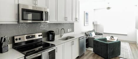 Una cocina moderna con electrodomésticos de acero inoxidable, armarios blancos y salpicadero de azulejos grises.