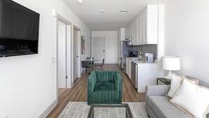 A modern kitchen with white cabinets, a dining area with a green chair, and a gray sofa.