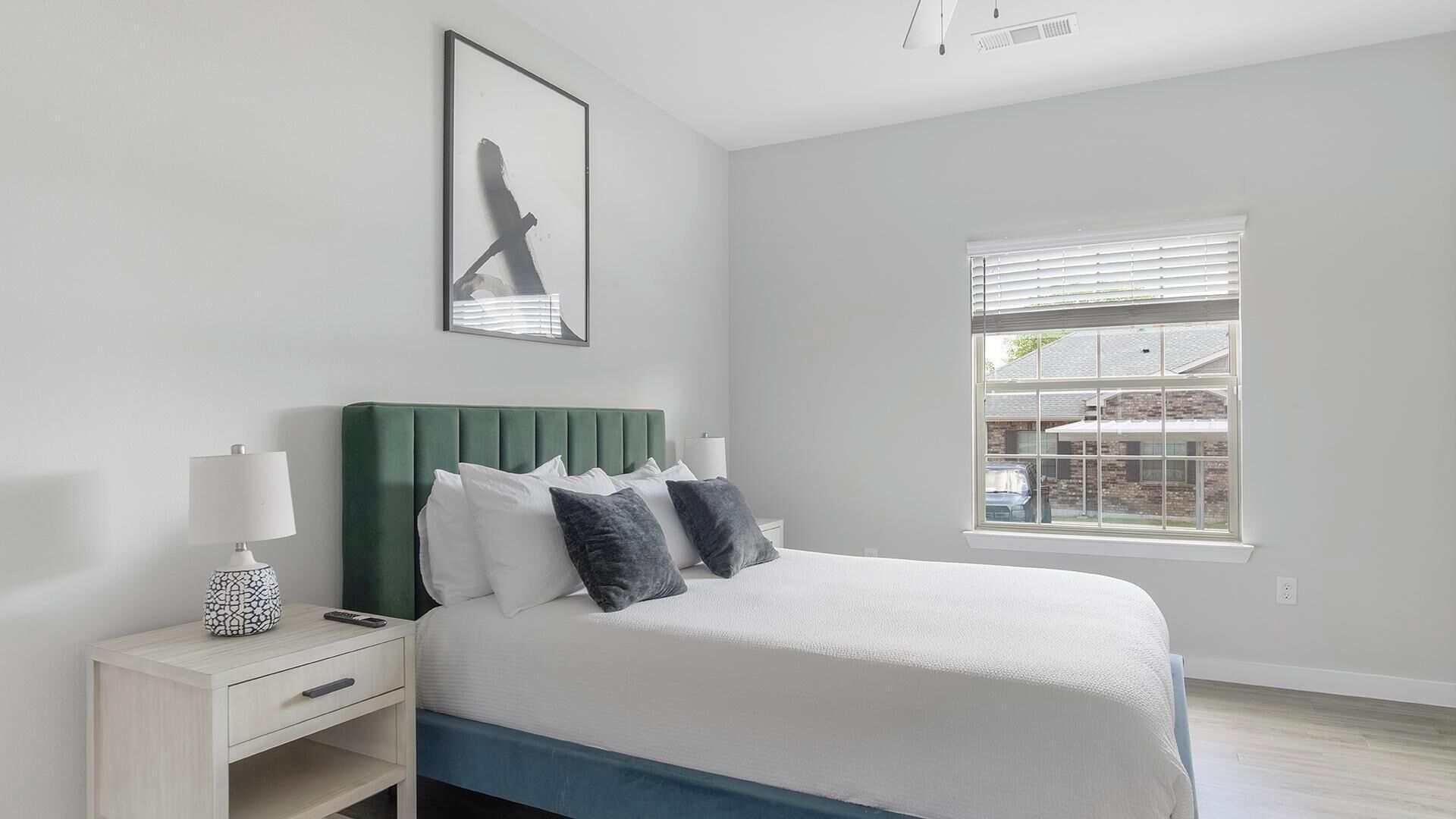 A bedroom with a bed, bedside tables, a window, and a painting on the wall.