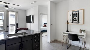 A modern kitchen with a granite countertop, black cabinets, and a built-in sink. There's a dining area with a white table and black chairs, and a framed vintage camera on the wall. - Landing | Modern 1BD, Yoga Studio, Clubhouse (Dallas)