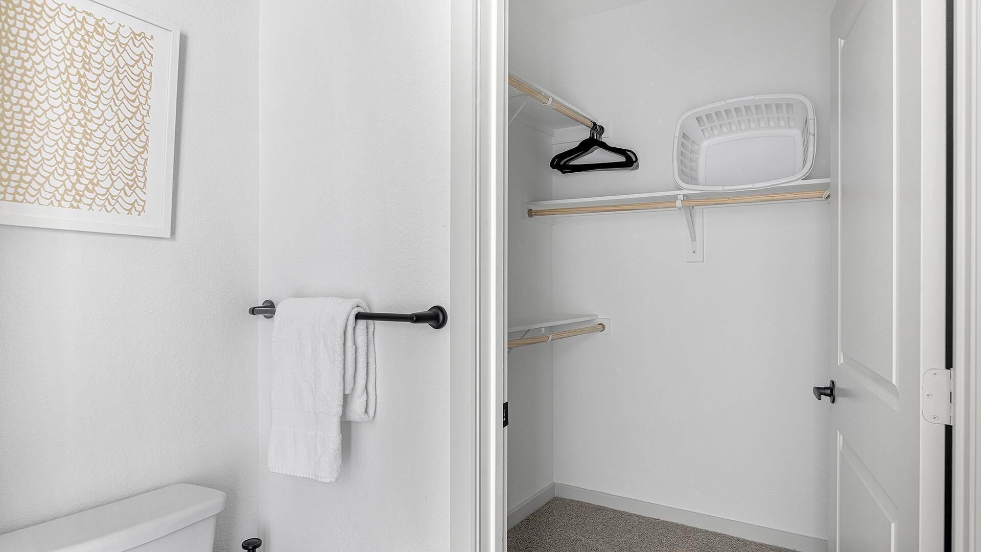 A bathroom with a toilet, a towel rack with a towel, a shower area with a shower caddy, and a shelf with a hanging rack.