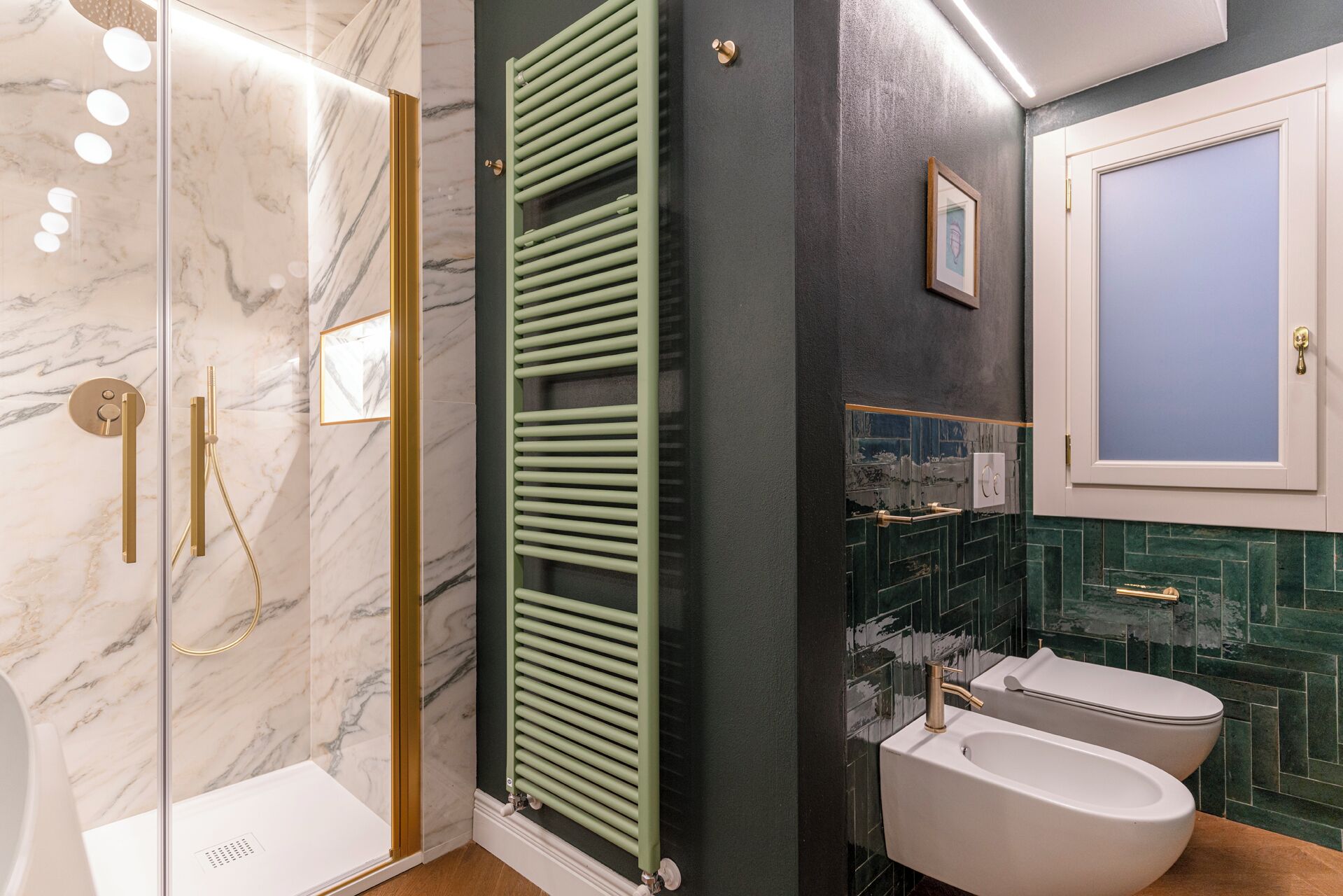 A bathroom with a glass shower enclosure, a green towel rack, a white toilet, and a bidet.