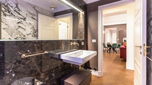 A modern bathroom with a large mirror, two sinks, and a bench.