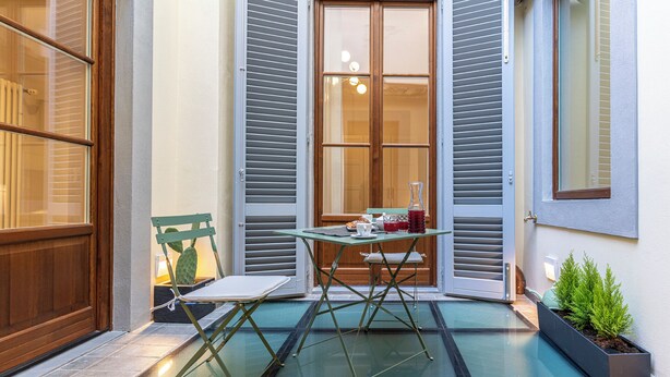 A small outdoor seating area with a table and chairs, a cactus, and a potted plant.