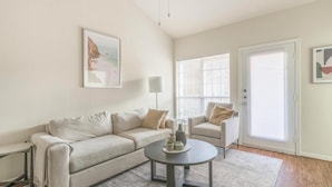 A living room with a beige sofa, a round coffee table with decorative items, a floor lamp, and a painting on the wall.