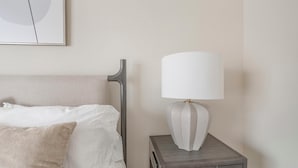 A neatly made bed with a grey headboard, a white pillow, and a grey nightstand with a white lamp.