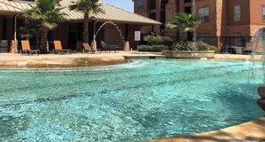A clear pool with lounge chairs and a covered area, surrounded by brick buildings and palm trees. - Landing | Stylish 2BD, Clubhouse, Gym (Pasadena)