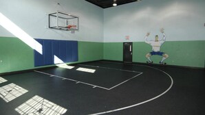 Een binnenshuis basketbalveld met een basketbalring, veringswanden en een deur.