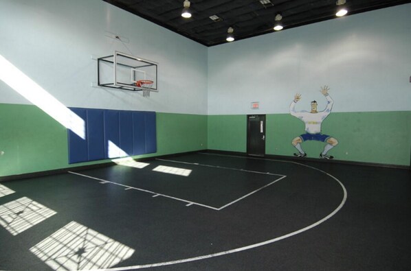 An indoor basketball court with a basketball hoop, padded walls, and a door.