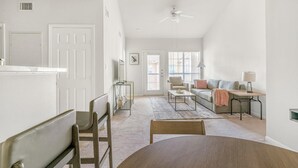 A spacious living area with a dining table, chairs, a sofa, and a coffee table. There is a door leading to another room and a window with blinds. - Landing | Spectacular 2BD, Pool, Game Room (Pasadena)