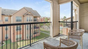 A balcony with wicker chairs, a view of neighboring buildings, and a clear sky. - Landing | Spectacular 2BD, Pool, Game Room (Pasadena)