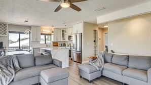 A modern living room with grey sofas, a ceiling fan, and a kitchen in the background. - Outdoor Oasis w/ Boat Slip & Spa in St Augustine! (St. Augustine)