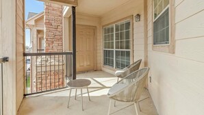 A covered balcony with a table and two chairs, a door, and a window with blinds. - Landing | Chic 2BD, Clubhouse, Game Room (Pasadena)