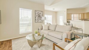 A living room with a glass coffee table, beige sofa, and a dining area with a metal chair. - Landing | Chic 2BD, Clubhouse, Game Room (Pasadena)