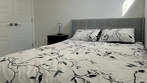 A bedroom with a bed, a nightstand, a lamp, and a door. - Newly legal 2BR Basement in Seton, SE Calgary- weekly/monthly discount (Calgary)