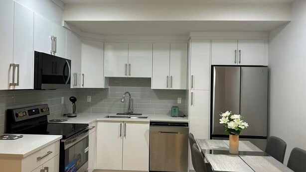 A modern kitchen with white cabinets, stainless steel appliances, a built-in microwave, and a dining area with a table and chairs. - Newly legal 2BR Basement in Seton, SE Calgary- weekly/monthly discount (Calgary)