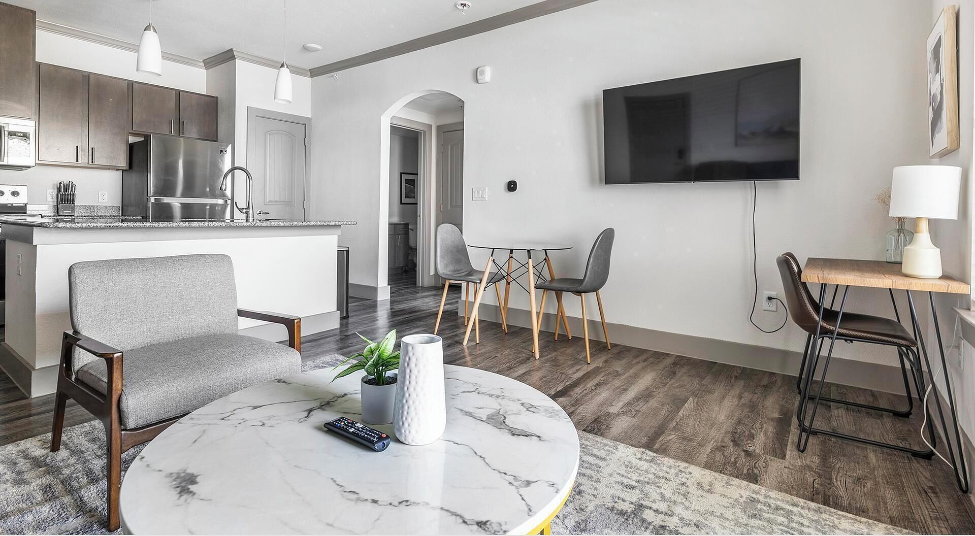 Ein modernes Wohnzimmer mit einem Marmortisch, einem grauen Sofa und einem Essbereich mit an der Wand montiertem Fernseher.