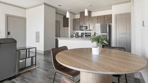 A modern kitchen with stainless steel appliances, a dining area with a round table and chairs, and a gray sofa in a living room. - Landing | Spectacular 1BD, Courtyard, Gym (Manor)