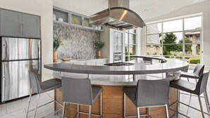 Une cuisine moderne dotée d’un îlot central, d’appareils électroménagers en acier inoxydable et d’une grande fenêtre offrant une vue sur l’extérieur.