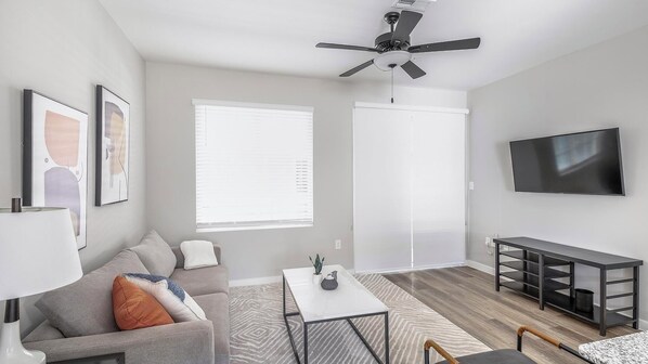 Un salon moderne avec un canapé, une table basse, un téléviseur et un ventilateur de plafond.